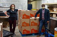 image of two OU employees standing in a warehouse-style room with big boxes and wearing masks